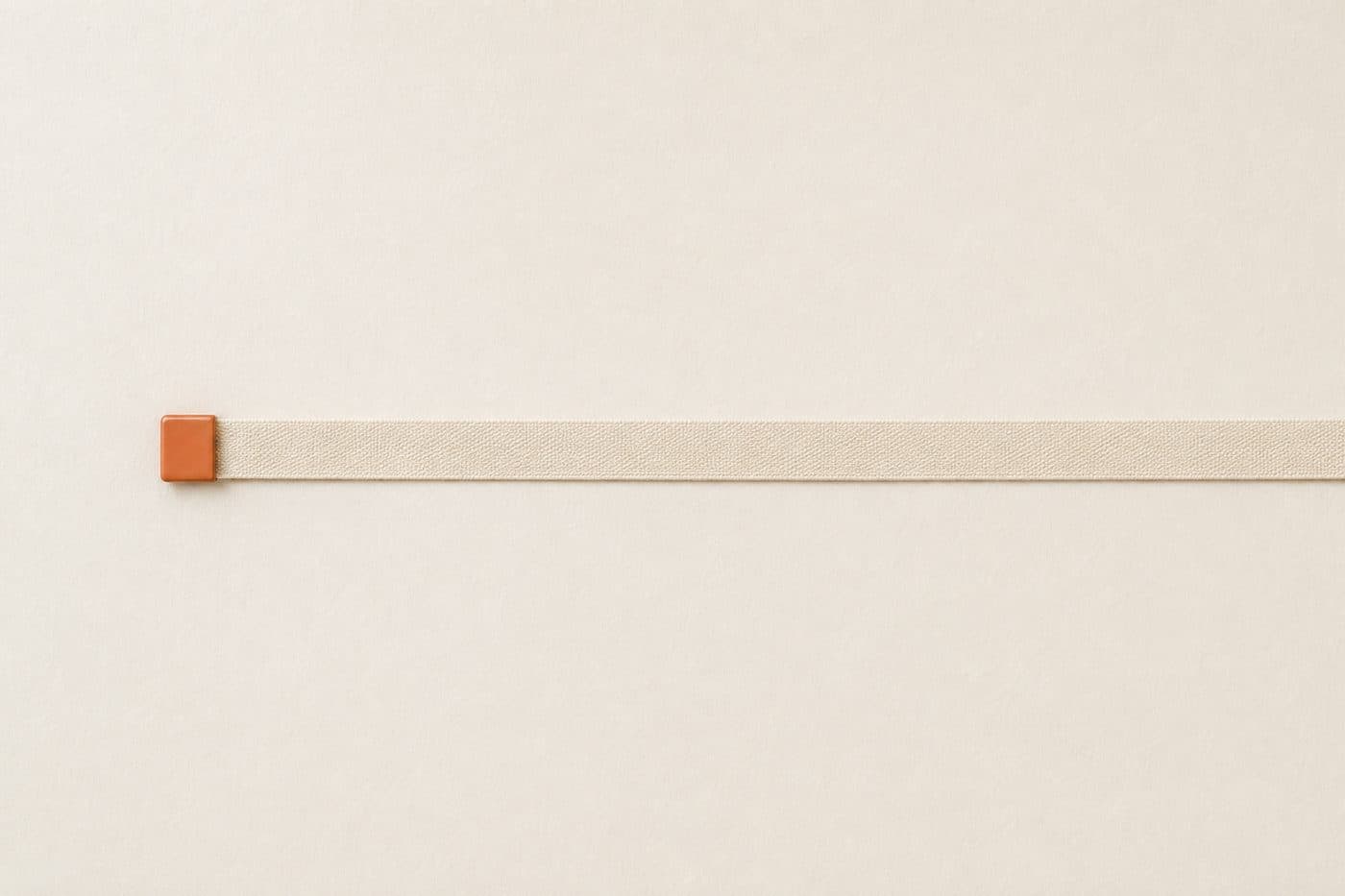 A plain cloth tape lying straight across paper with a small orange marker at its starting end.